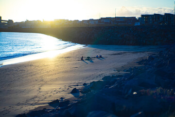 Sunset beach with people relaxing on sand near city coast