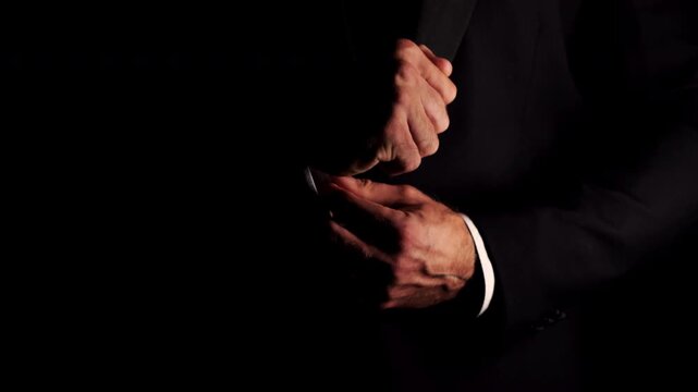 Close up of an elegant man in a suit adjusting cufflinks in a dark interior.