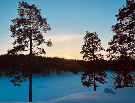 Sunset over frozen winter lake with snowy forest in Norway