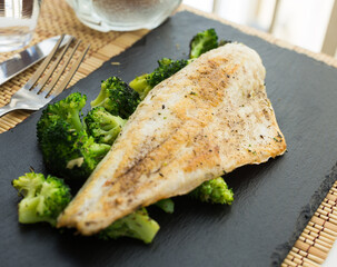 fried fillet of sea bass with garnish of broccoli on black warm stone plate
