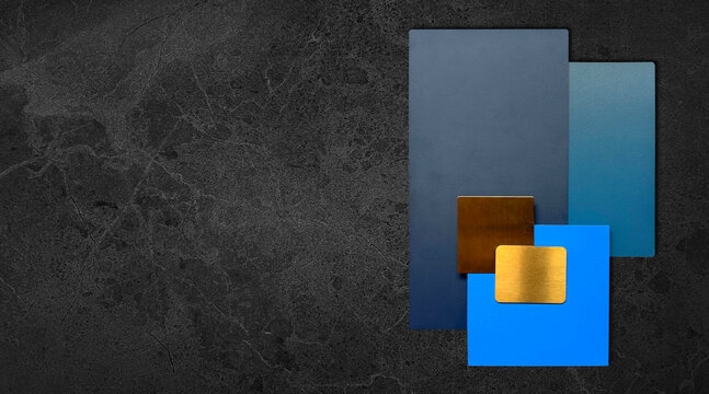 interior materials samples including solid blue laminated, blue painted wood, gold brushed metallic stainless placed on dark black marble table background.