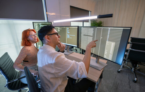 Two developer focus on coding at their desk, surrounded by multiple computer screen displaying line of code in a contemporary workspace, enhancing teamwork and creativity. - Powered by Adobe
