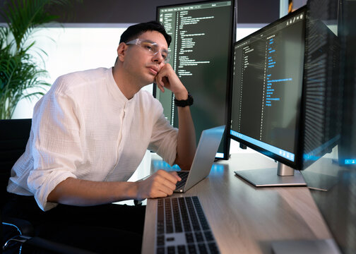 Tired programmer working at a modern desk surrounded by multiple monitor during a busy day in a bright office space