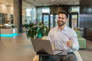 Like. Happy young businessman guy working on laptop looking approvingly at camera showing thumbs up, like sign positive something good, positive feedback sitting in modern office lobby. Businesspeople
