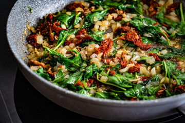 Frying spinach, onion and sun dried tomatoes in frying pan - cooking creamy Tuscan sauce