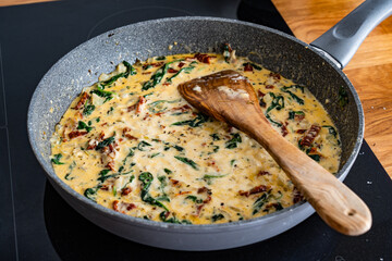Cooking creamy Tuscan sauce with parmesan cheese, spinach and sun dried tomatoes in frying pan