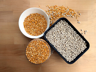 White beans in a black container and small, yellow, split peas in a clear container and in the white bowl. Wooden background