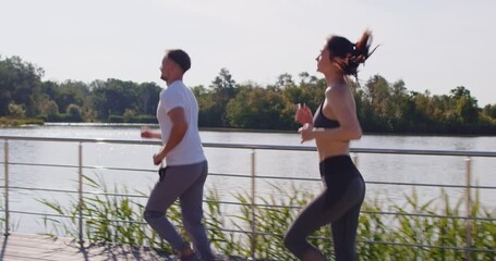 Couple having active day, jogging along river or lake during summer day, running in morning, being motivated for keeping fit and staying healthy, enjoying sporty activity together.