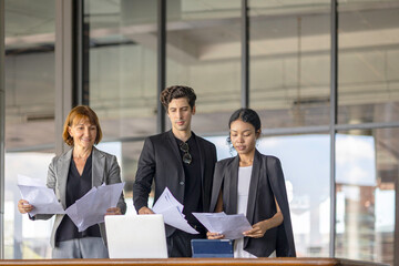 A group of business workers from different generations celebrate great deal by throwing papers to the sky in an office. Moment of happiness among coworkers after solving business challenges.