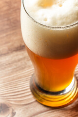 Glass of beer with thick foam on top, placed on a wooden surface with warm lighting.