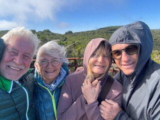 Joyful group of senior friends enjoying trekking in mountain in a sunny windy day, four mature people looking at camera smiling. Sport, freedom, healthy lifestyle concept