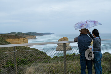  A woman holds an umbrella for her partner as he takes photos of the Twelve Apostles along the Great Ocean Road in Victoria, Australia, on a cloudy day.