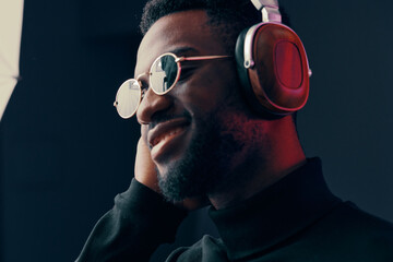 Young Black man enjoying music with headphones, wearing stylish sunglasses and a black turtleneck, with a vibrant background reflecting joy and style