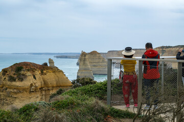  A woman holds an umbrella for her partner as he takes photos of the Twelve Apostles along the Great Ocean Road in Victoria, Australia, on a cloudy day.