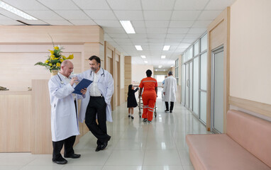 Two doctor in white coat review paperwork at a reception area while patient and nurse move through a bright, contemporary hospital corridor.