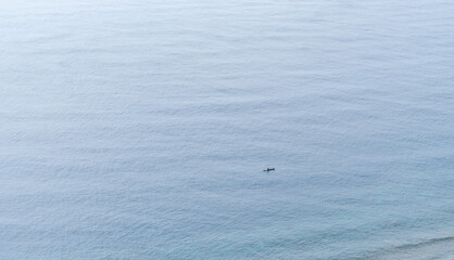 Minimal aerial view of a calm blue ocean with a small lonely boat in the middle, evoking feelings...