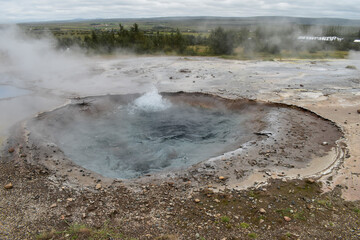 Bubbling water in a geyser lake, steam coming out of it, landscape
