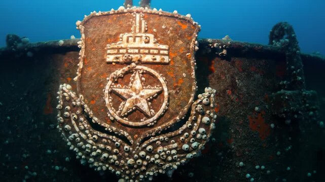 Wreckage emblem on a ship underwater covered in barnacles, shipwreck site, diving, marine life.