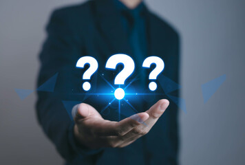 Businessman hand holding glowing question mark icons, symbolizing uncertainty, decision making, problem solving, FAQ, support, innovation, and future strategy in corporate concept.