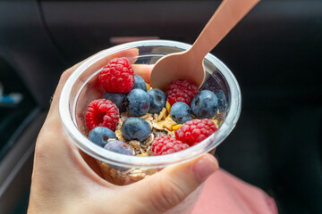 Close-up of a hand holding a cup of granola with blueberries, raspberries, and yogurt. Concept of healthy lifestyle, breakfast, and organic food