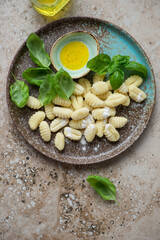 Plate with uncooked italian potato gnocchi on a beige granite background, vertical shot, above view