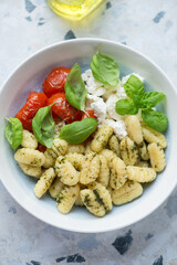 Italian gnocchi with roasted tomatoes, ricotta cheese and fresh basil in a plate, vertical shot, middle closeup
