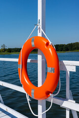 Orange swimming rescue wheel hanged on the rails of the white jetty. Safety equipment on the water bank