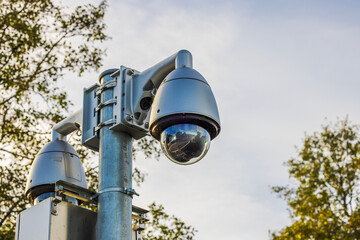 Close-up view of surveillance camera on metal pole with reflection on lens against autumn sky and trees. Sweden.