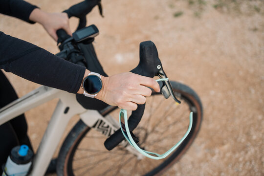 Young woman cyclist wearing smartwatch holds gravel bike handlebars