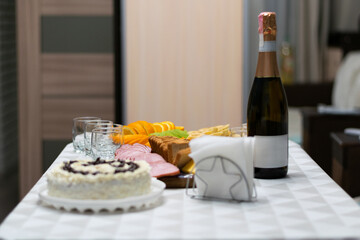 Festive table with cake, champagne, glasses, sliced fruits, cheese, bread, and snacks prepared for holiday party or celebration