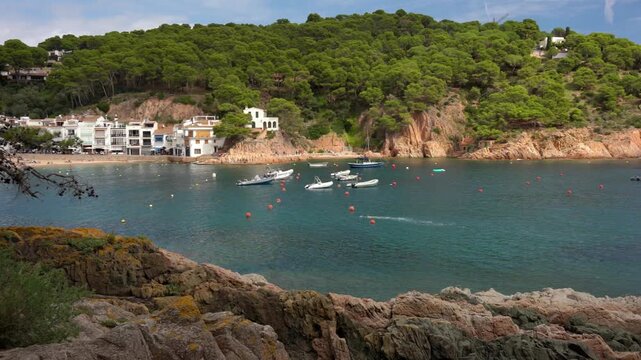 Scenic coastal village of Aiguafreda in Begur, Spain, with moored boats in a turquoise bay surrounded by rocky cliffs and pine trees