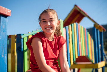 Smiling child girl playing on a colorful playground structure in a sunny park, enjoying a fun and active outdoor moment.