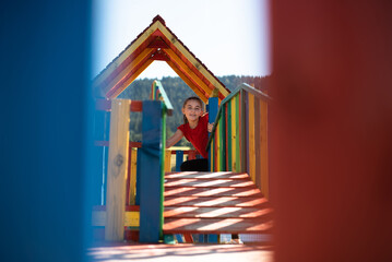 A happy child girl playing on a colorful playground structure in a sunny park, enjoying a fun and active outdoor moment.