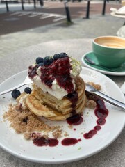 Stack of pancakes with whipped cream, blueberry sauce and fresh berries served with coffee