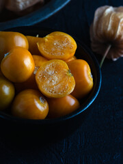 Close-up of fresh golden berries, also known as physalis or ground cherries, in a black bowl on a dark textured background.