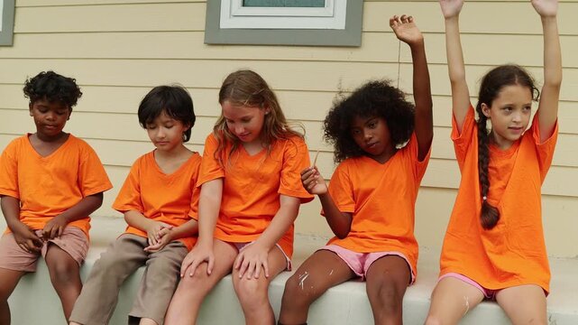 Group young male and female international school students sit in a row eating popsicles to cool down and enjoy their favorite delicious cool ice cream after playing outdoor sports during the summer.