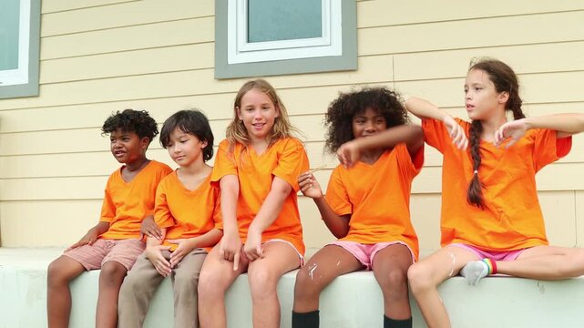 Group young male and female international school students sit in a row eating popsicles to cool down and enjoy their favorite delicious cool ice cream after playing outdoor sports during the summer.