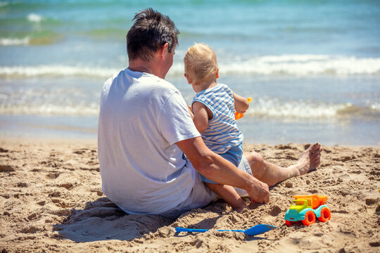 A happy grandfather and his little grandson are playing on the beach. Grandfather is holding the child in his arms
