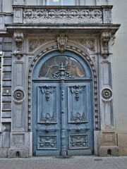 Obraz premium Rustic Blue Door on a Historic Facade - An ornate, rustic blue door with intricate carvings and an arched transom on a weathered stone building in Ghent, Belgium.