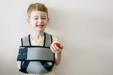 A boy with a bandage on his shoulder is eating an apple. Fracture of the collarbone or arm.