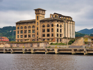 Abandoned old factory by the Bilbao river. - The abandoned Forjas de Zorrozaurre building and industrial ruins by the Nervión River in Bilbao, Spain, under a cloudy, moody sky.