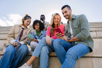 Group of young multiracial students sharing a moment outdoors while looking at a smart phone screen. Youth community, friendship and lifestyle concept.