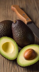 Still life of avocados with one sliced in half and a knife on a rustic wooden surface background