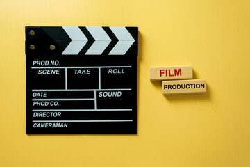 Naklejka premium Black movie clapperboard with wooden blocks showing text Film Production on yellow background, concept of filmmaking, cinema industry, and creative media.