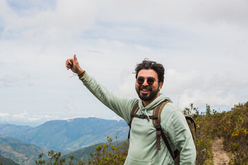 Latino man hiking in the Santurban moor in Colombia, smiling with backpack and giving thumbs up, symbolizing adventure, eco tourism, outdoor lifestyle, travel freedom, exploration health and happiness