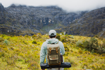 Latino man with backpack exploring Santurban moor in Colombia, standing in front of foggy mountains and wilderness, representing hiking, eco adventure, outdoor lifestyle, freedom, discovery and nature