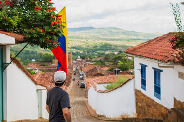 Latino man walking through colonial streets of Barichara Colombia, admiring traditional architecture and Colombian flag, representing culture, identity, travel lifestyle, heritage and exploration
