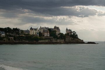 Fototapeta premium Coastal view of Dinard, France, showing historic seaside mansions under a dramatic cloudy sky. Classic French architecture meets the ocean in a quiet and moody atmosphere.