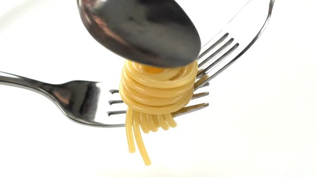 A fork is wrapped in spaghetti with a spoon pressing down on the food