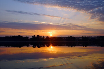 Beautiful moments of sunrise. Shot from the surface of the lake, the shore and trees against the beautiful sky. Morning fog. Reflection on the surface of the water.